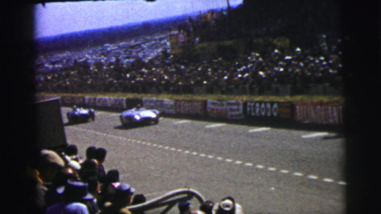 1954 Le Mans spectator-shot frame showing a race car on the circuit, foreground spectators, trackside boards, and packed stands.