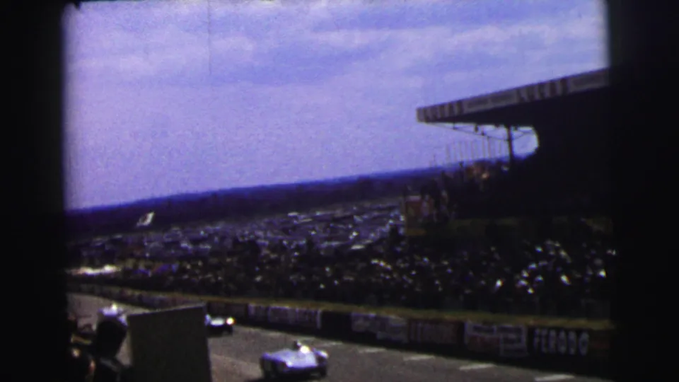 1954 Le Mans race cars pass below crowded grandstands in a grainy 8mm spectator-shot frame.
