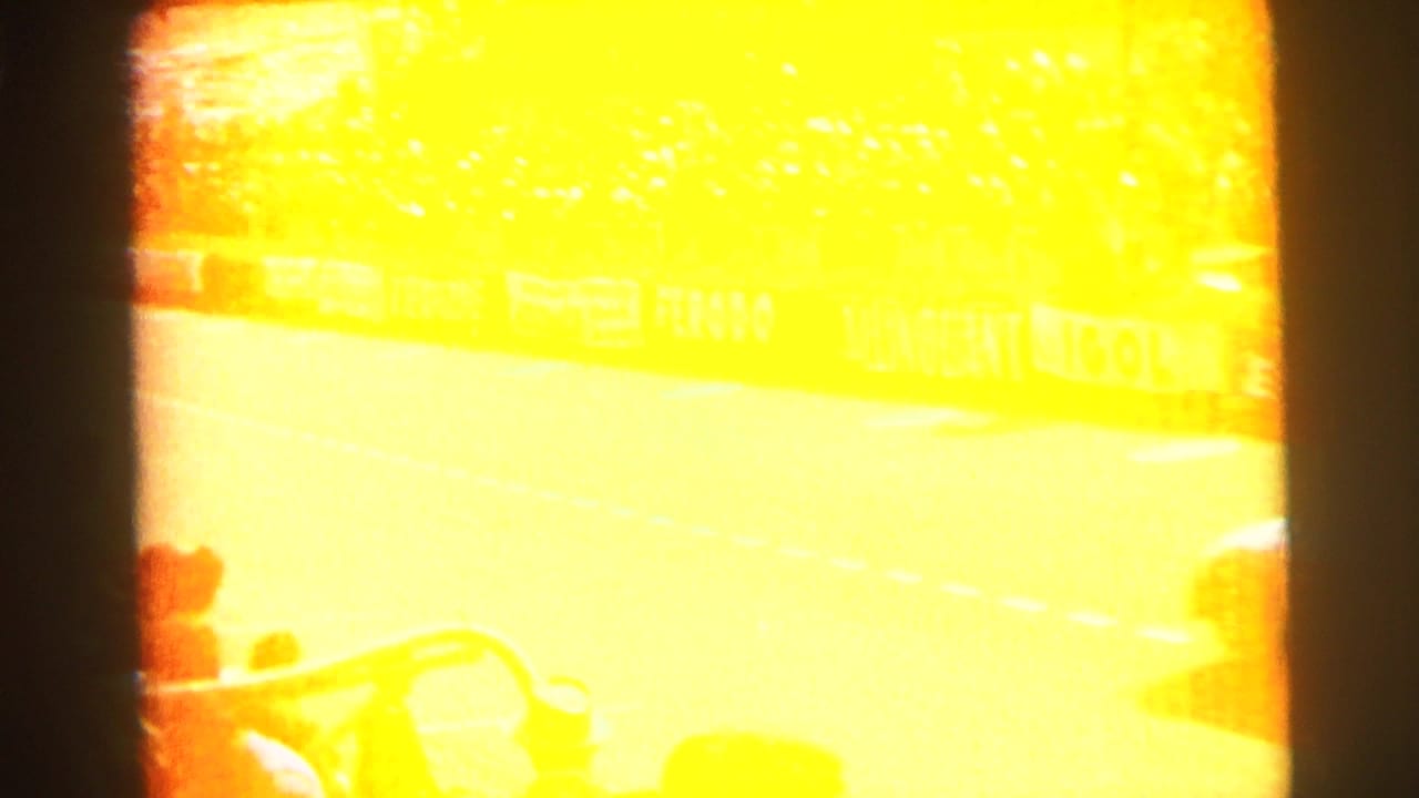 A bright overexposed 8mm frame from the Le Mans footage partially obscures the track, crowd, barriers, and a vehicle at the edge.