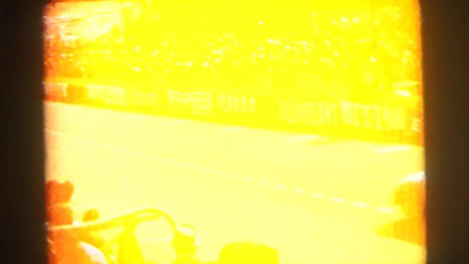 A bright overexposed 8mm frame from the Le Mans footage partially obscures the track, crowd, barriers, and a vehicle at the edge.
