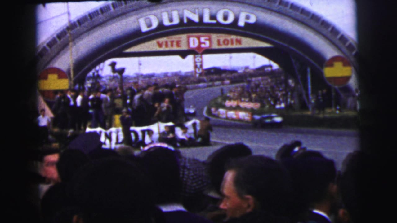 1954 Le Mans crowd watches cars pass under the Dunlop bridge from a trackside home-movie viewpoint.