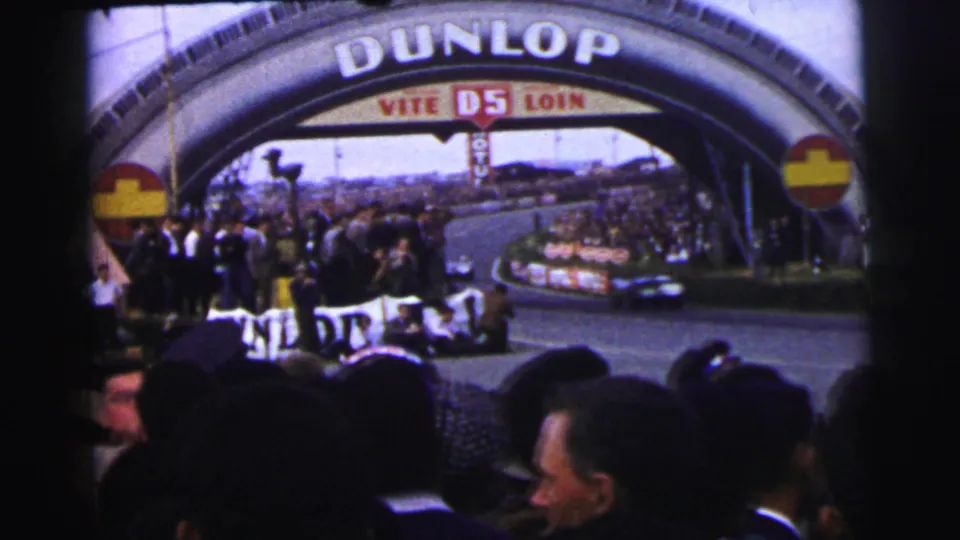 1954 Le Mans crowd watches cars pass under the Dunlop bridge from a trackside home-movie viewpoint.