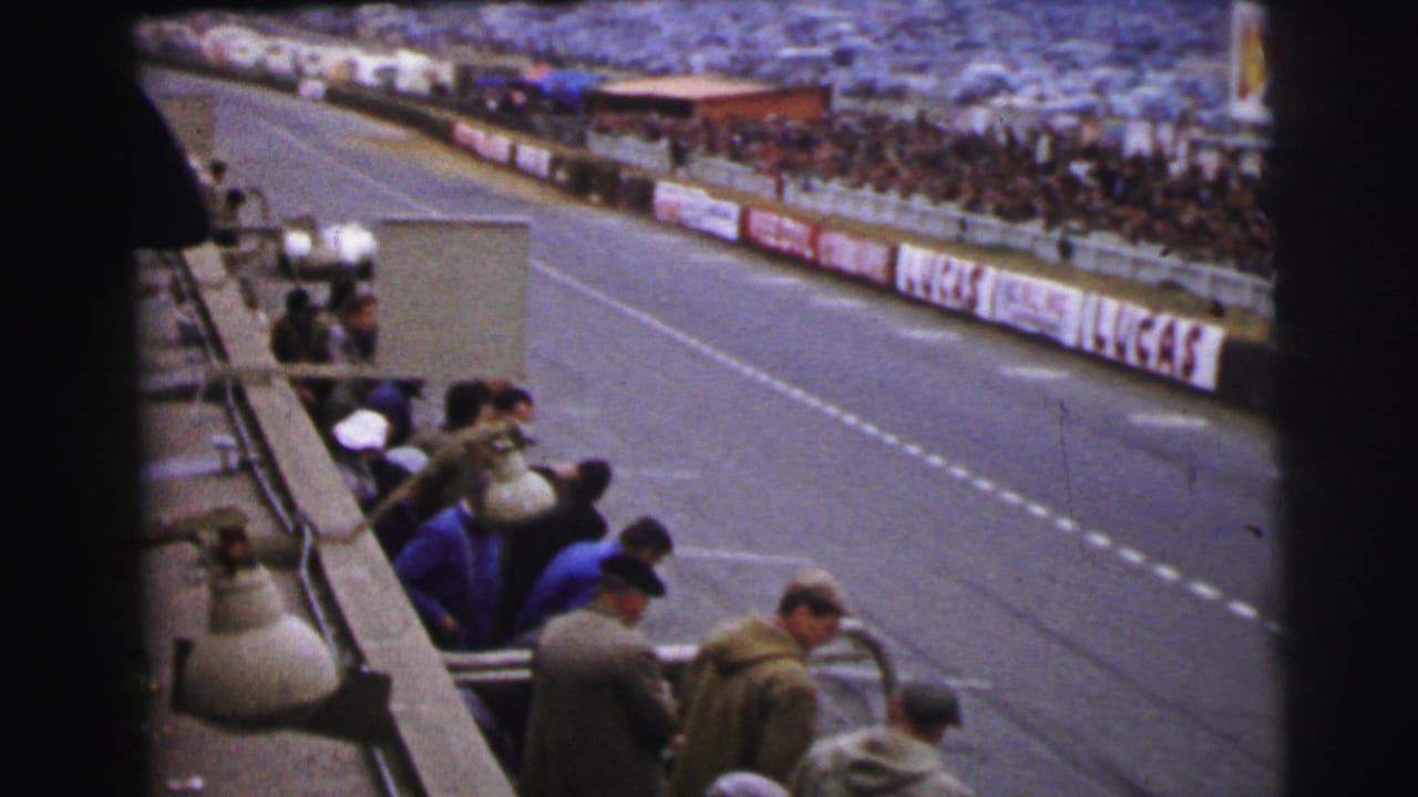 1954 Le Mans home-movie frame showing a trackside spectator view before the white race car reaches the pit lane.