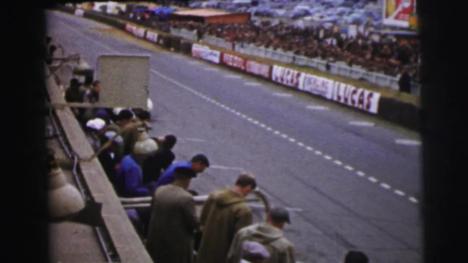 Spectators at Le Mans look down toward the pit lane as the open track and sponsor banners fill the frame.