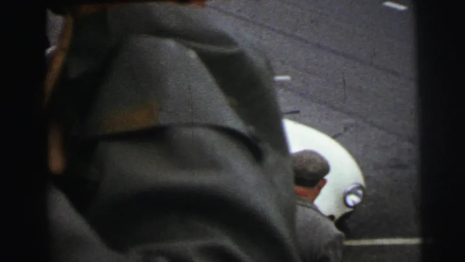 A foreground spectator partly obscures the Le Mans track view as a white race car and several caps remain visible below.