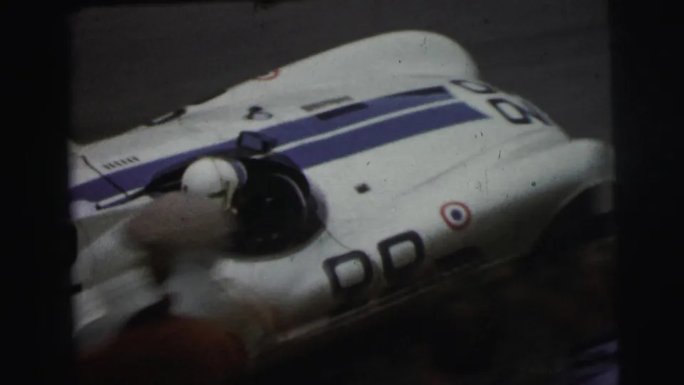 Close view of a white and blue race car at Le Mans, France, with soft 8mm grain and a blurred spinning front detail.