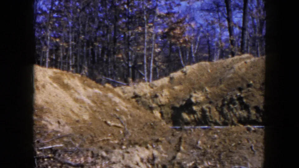 1954 Hicksville home-movie frame showing disturbed earth, a dirt mound, tire ruts, and bare trees beyond the excavation area.