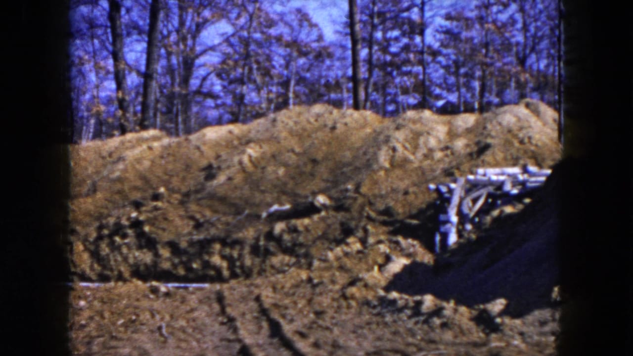 1954 Hicksville, New York 8mm frame showing a dug construction area with earth piles, bare trees, and scattered lumber.