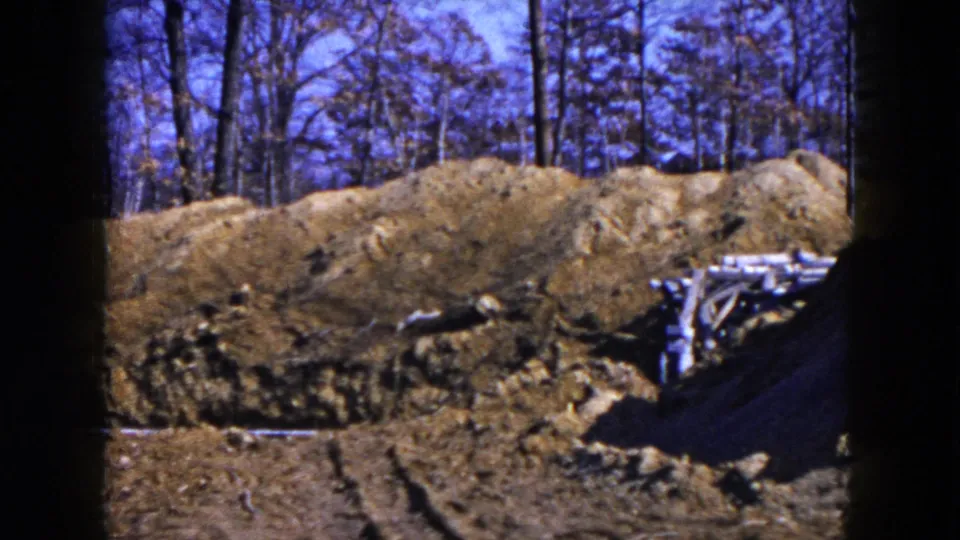 1954 Hicksville, New York 8mm frame showing a dug construction area with earth piles, bare trees, and scattered lumber.