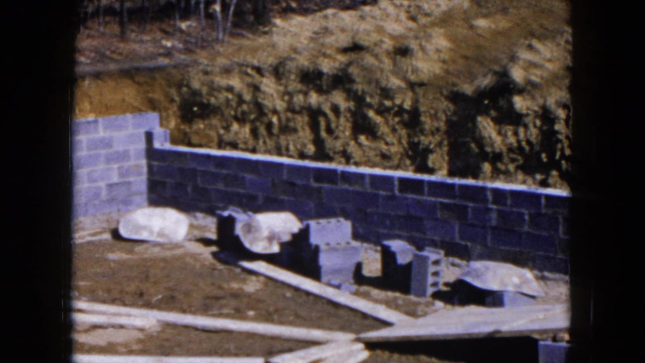 Cinder block foundation wall beside a dirt embankment with blocks and planks on bare ground.
