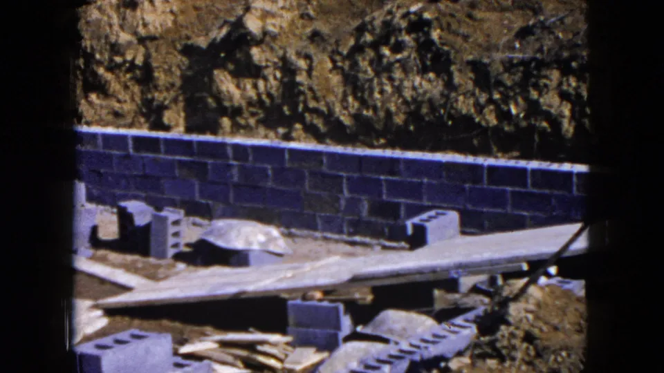 The camera pans across a Hicksville foundation site, showing cinder block work, planks, loose blocks, and rough excavated ground.