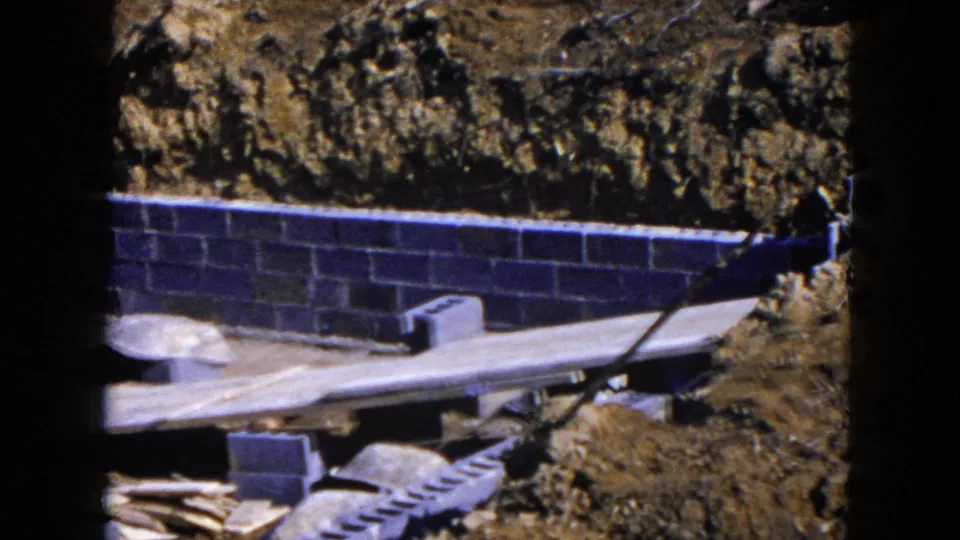 Late frame from the 1954 Hicksville construction pan with a cinder block foundation, earth bank, lumber, and scattered site materials.