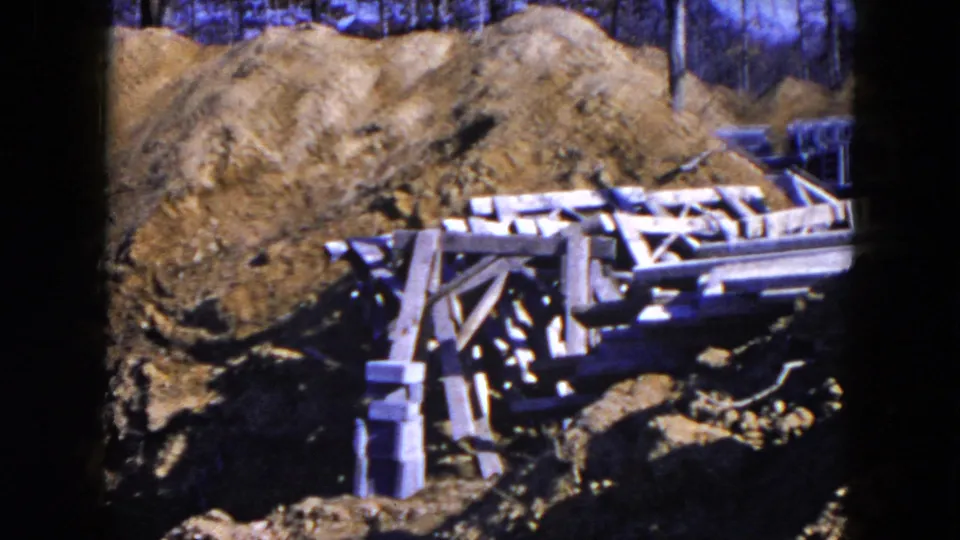 The later frame shows mounded soil, timber formwork and scattered boards in the Hicksville residential construction area.