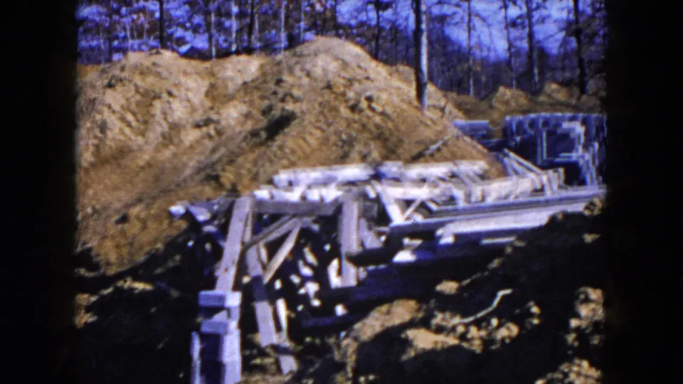 1954 Hicksville construction site with mounded soil, wood forms, concrete blocks, and leafless trees in the background.
