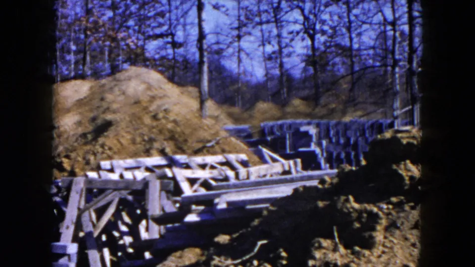 Hicksville, New York building lot in 1954 with dirt mounds, wood forms, concrete blocks, and wooded land beyond.