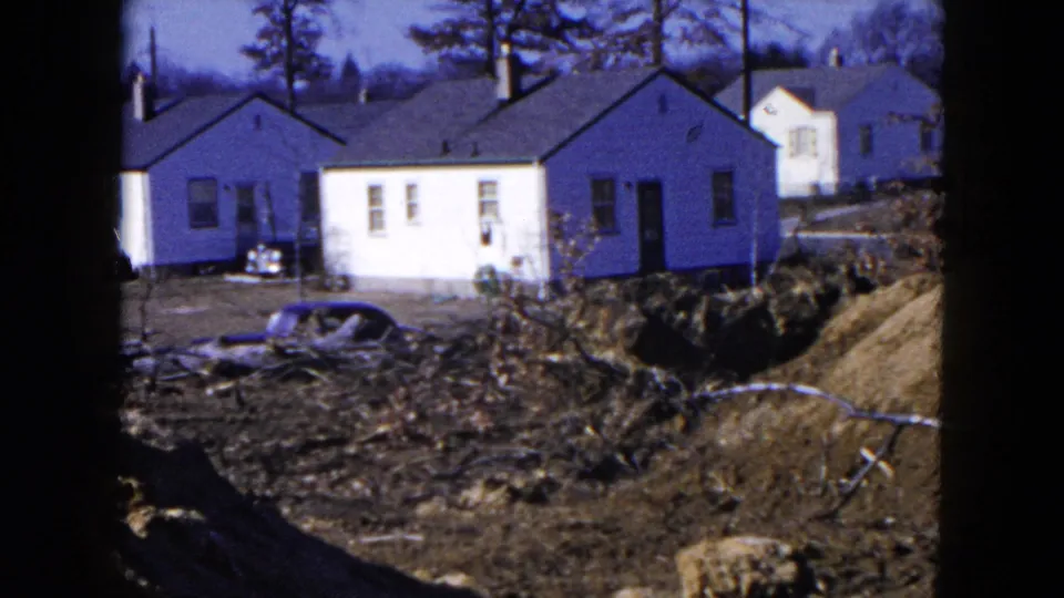 1954 Hicksville frame with light-colored bungalows, dirt piles, bare trees, and a car partly hidden by earthwork.