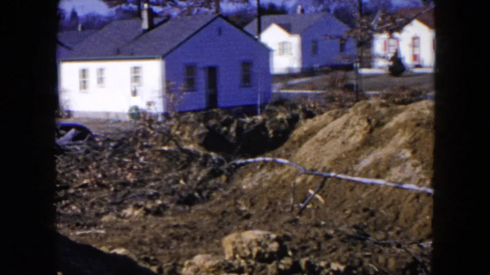 1954 Hicksville frame showing a small white house, background homes, exposed soil, and construction mounds.