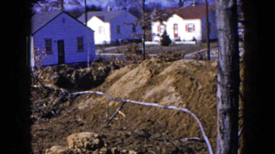 1954 Hicksville home-movie frame with small houses, bare trees, graded earth, and a prominent mound in front.