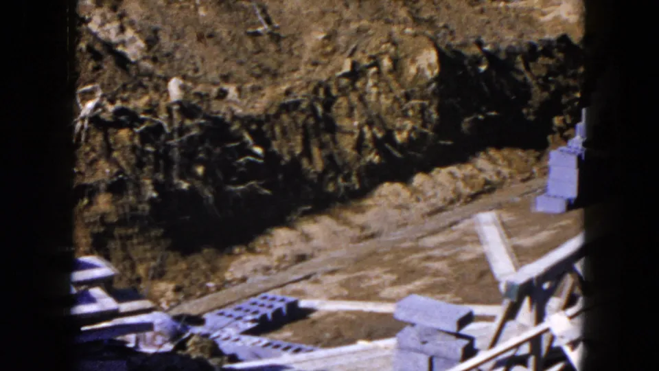 Cinder blocks and loose boards appear beside an excavated residential trench in the Hicksville construction footage.