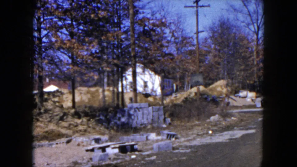 End frame from a 1954 Hicksville home movie showing blocks, dirt piles, trees, a utility pole, and residential buildings.