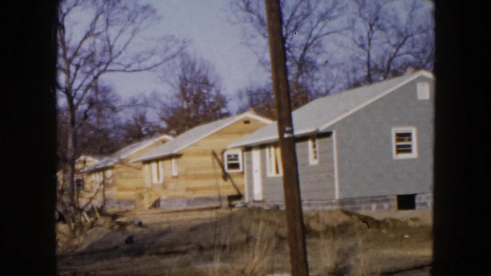 1954 Hicksville residential frame with a light wood-sided house, gray neighboring house, utility pole, and winter-bare trees.