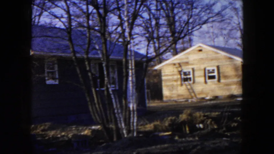 Home-movie frame from Hicksville in 1954 showing adjacent houses and residential construction through leafless trees.