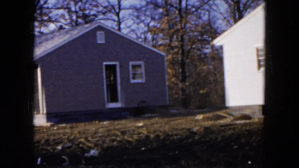 1954 Hicksville home-movie still showing a gray single-story house, doorway, window, porch edge, and nearby white house.