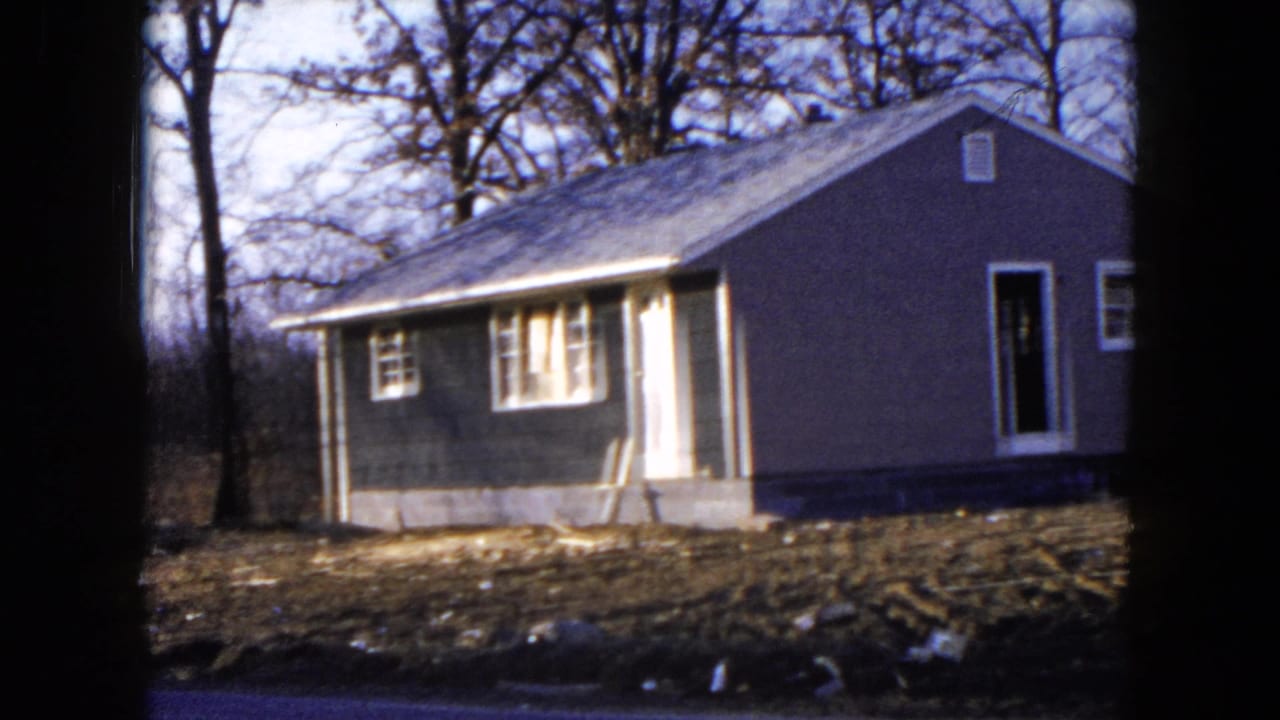 Small dark-sided house under construction beside bare trees.
