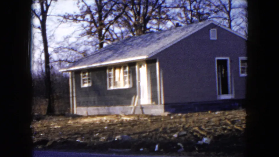 1954 Hicksville home-movie frame showing a small single-story house with porch supports and bare trees around the lot.