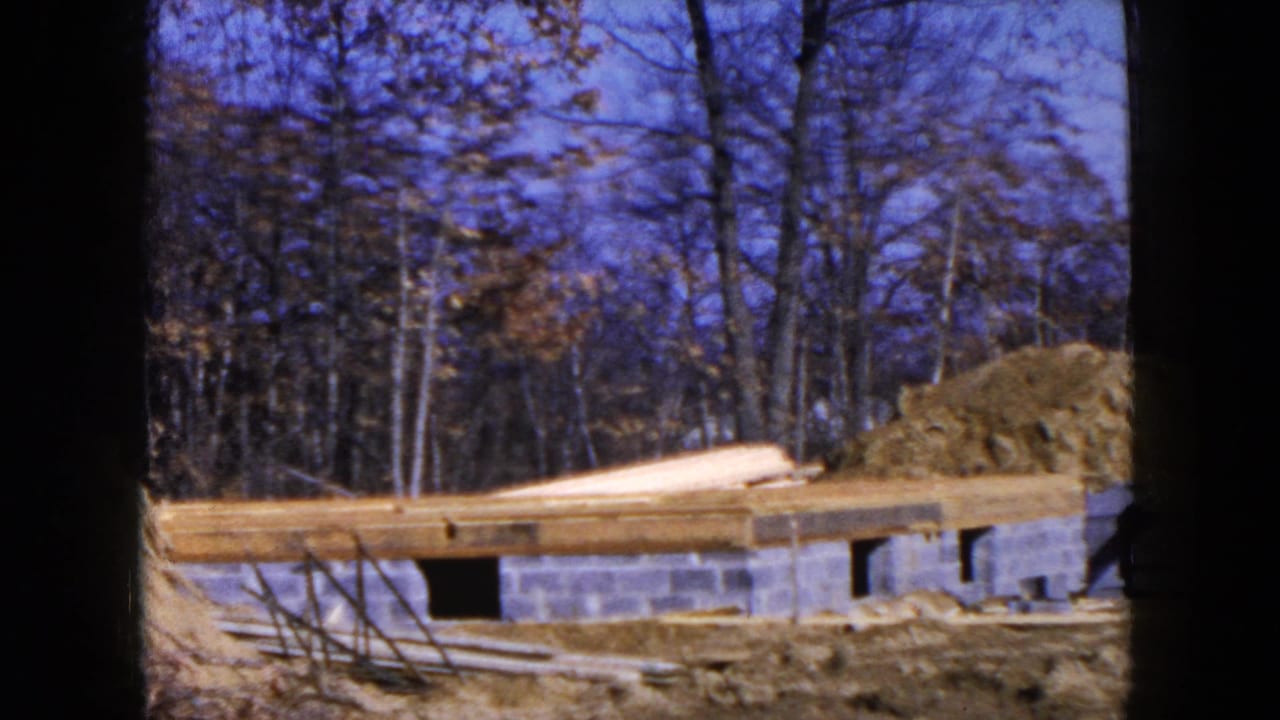 Concrete block foundation with lumber and dirt pile beside bare trees.