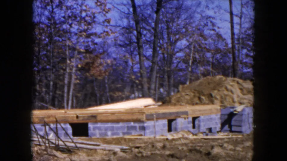 Hicksville, New York construction view with concrete block foundation, exposed joists, stacked boards, dirt mound, and winterlike trees.