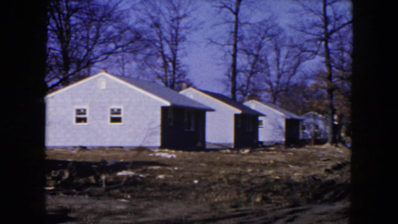 1954 Hicksville, New York home-movie frame showing white newly built houses, muddy lots and leafless trees.