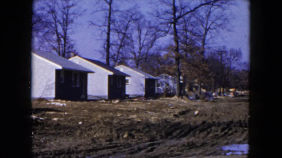 1954 Hicksville, New York frame with several white houses aligned beside an unpaved muddy road and winter trees.