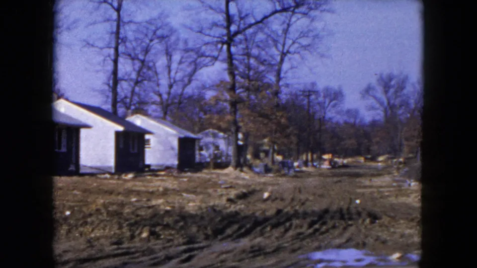 1954 Hicksville, New York home-movie view of houses at the edge of a muddy roadway with bare trees and open lots.