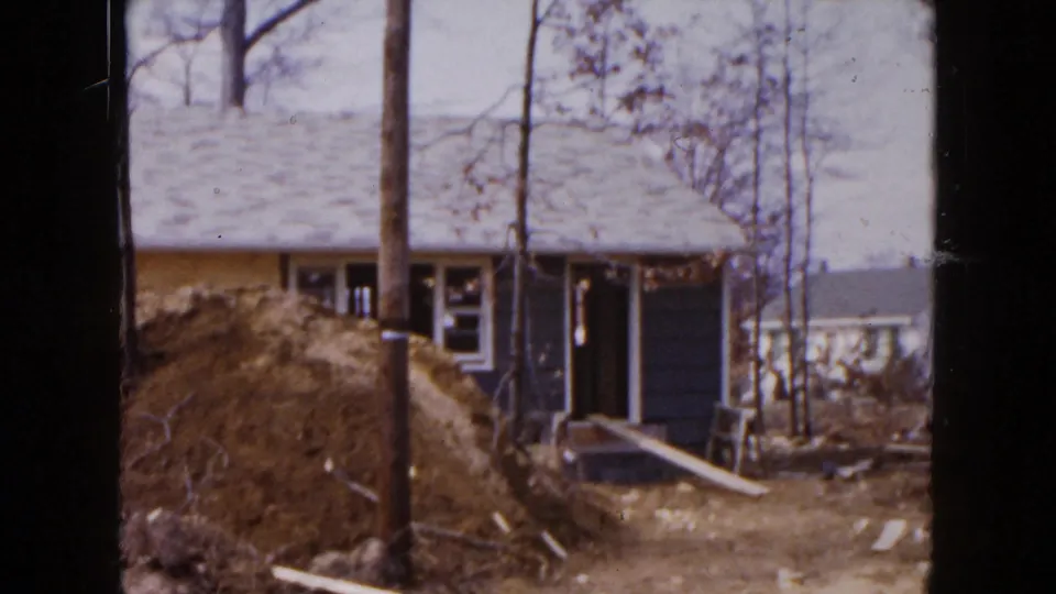 1954 Hicksville view of a residential construction site, showing the small house, dirt mound, trees, and scattered building materials.