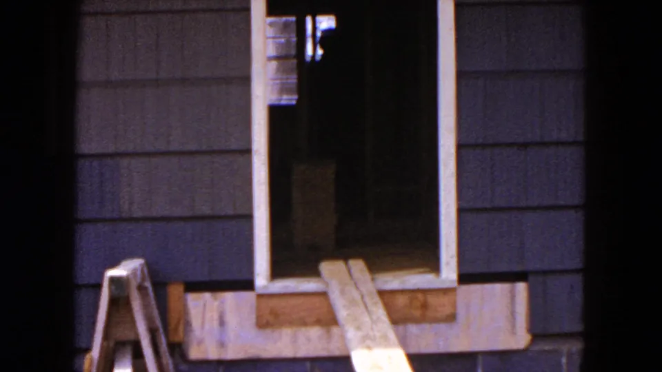1954 Hicksville frame of a house under construction, with a dark doorway, window trim, siding, and wooden boards near the base.