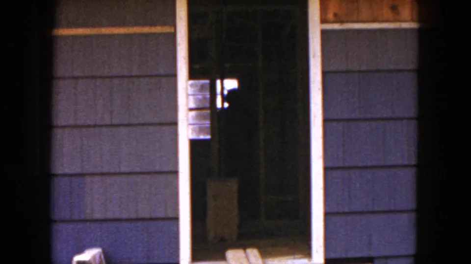 1954 Hicksville close view of an unfinished opening in a house exterior, with dark siding, wood trim, planks, and a sawhorse.
