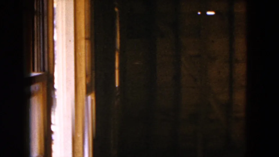 1954 8mm view inside an unfinished Hicksville home, with exposed wood framing and strong window light at the left edge.