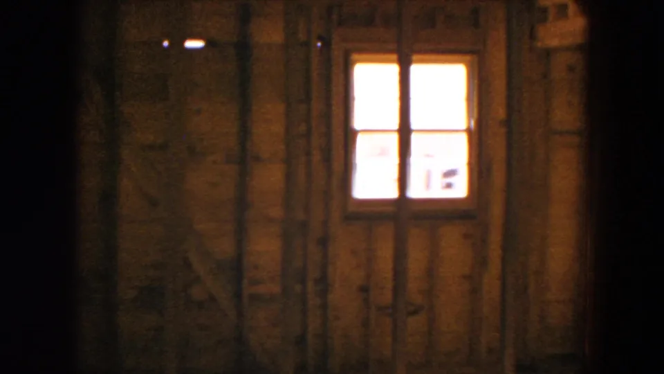A 1954 home-movie frame shows a small window set into exposed framing inside the unfinished Hicksville residence.