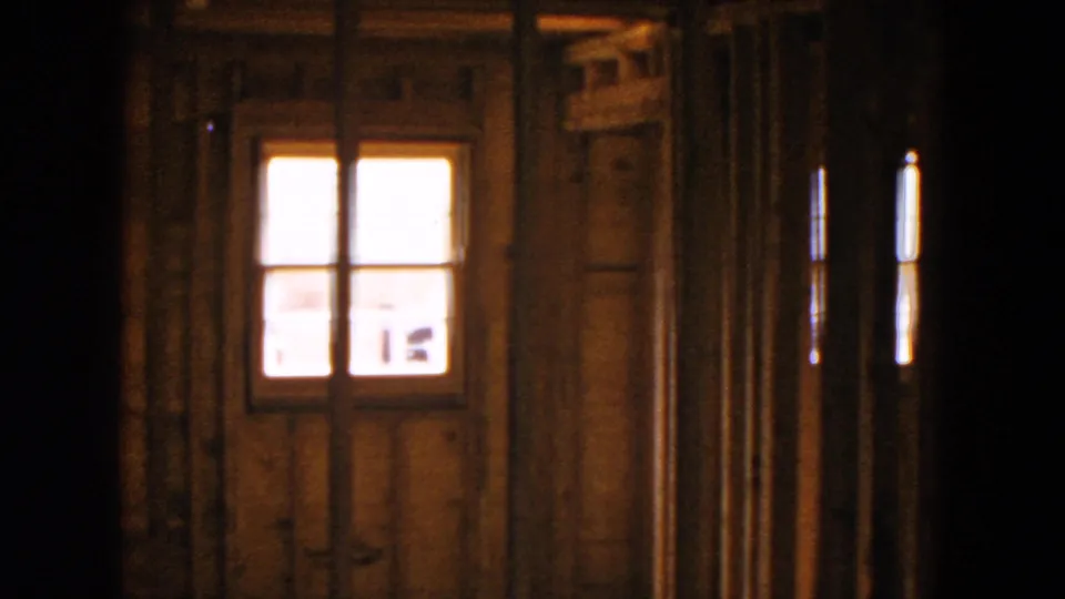 1954 Hicksville home-movie frame showing exposed wooden framing around a small glowing window inside an unfinished house.