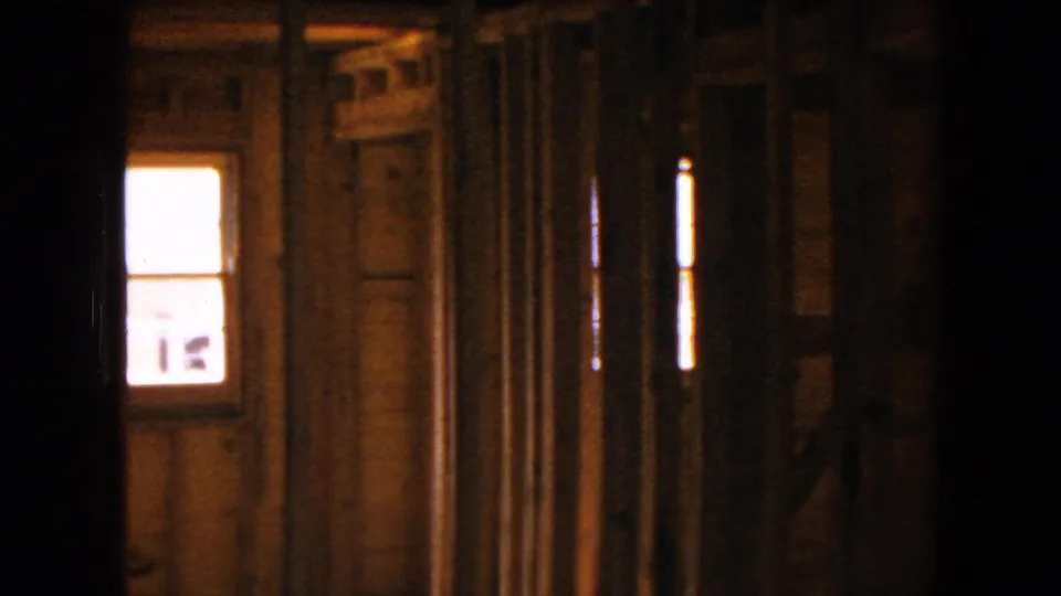 8mm frame from the Hicksville house interior, with a bright window and rough wooden framing visible in low light.