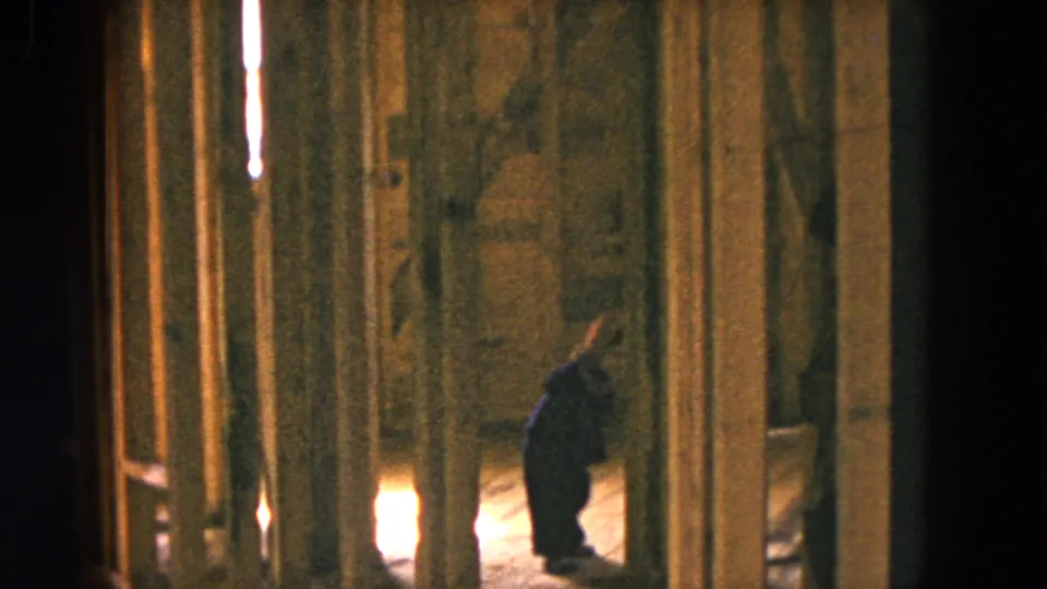 A child in dark clothing walks through the unfinished Hicksville interior, surrounded by exposed studs and warm low light.