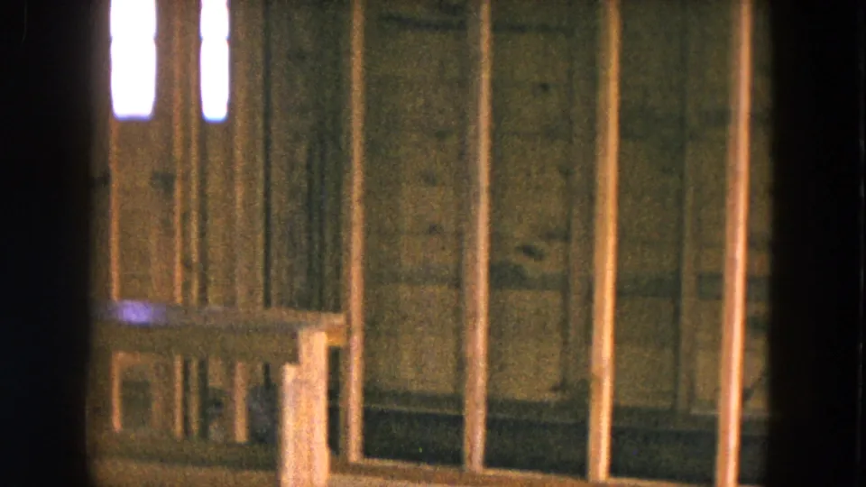 Interior framing of a Hicksville, New York house under construction, with vertical studs, rough sheathing, and a small wooden bench or box near the wall.