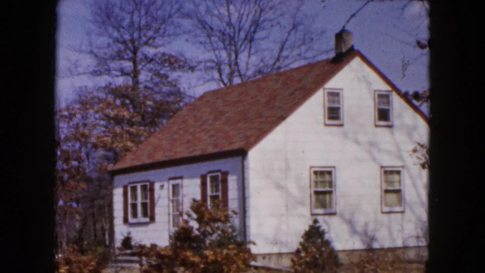 White two-story house in Hicksville, New York, framed by bare trees in a 1954 8mm home-movie shot.
