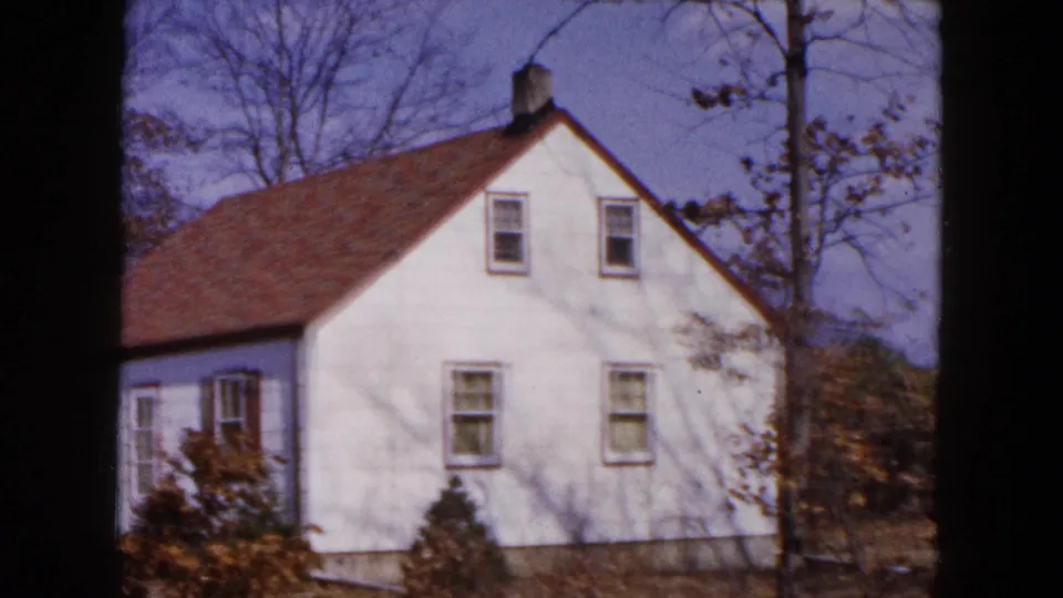 Closer 1954 Hicksville view of the white house facade, upper windows, shrubs, and bare trees.