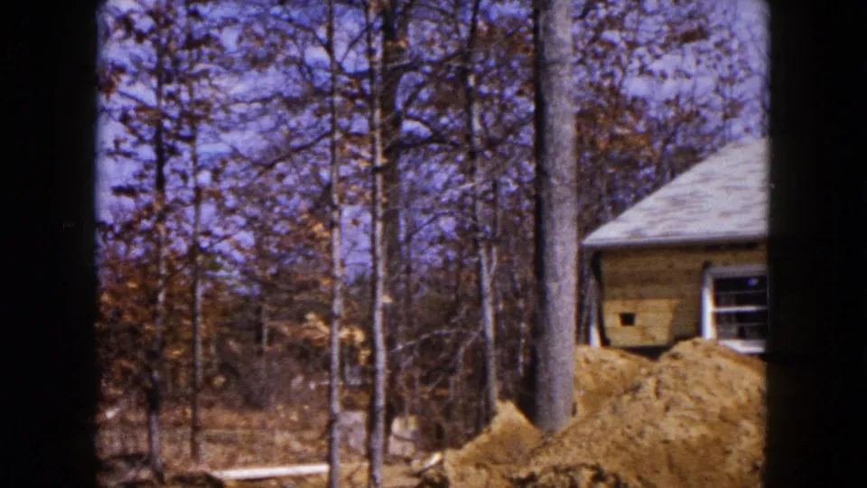 1954 Hicksville frame showing a partially built house near tall trees with mounded soil in front.