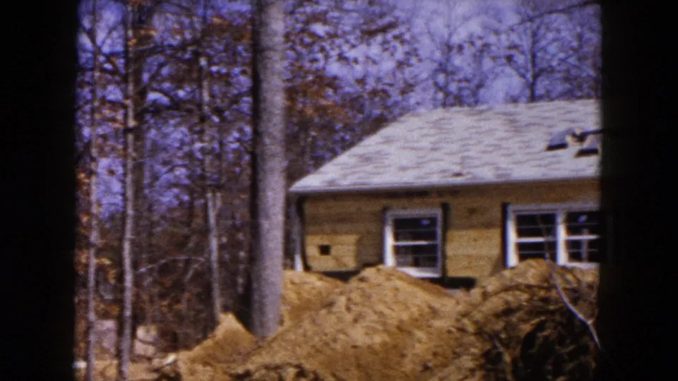 House construction in Hicksville, New York, with visible windows, roof, bare trees, and excavated soil in the foreground.