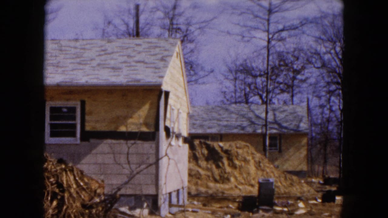 Damaged house beside a dirt pile with bare trees and debris in the yard.