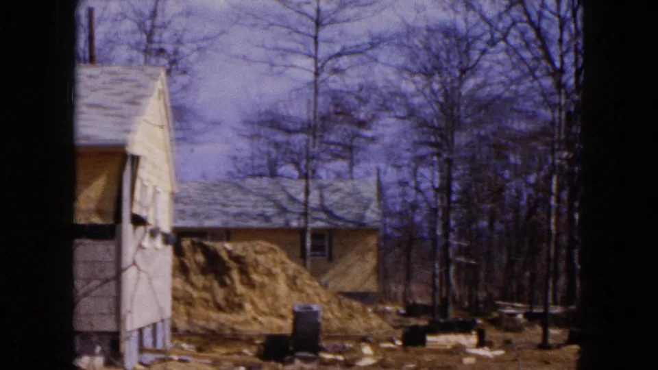 1954 Hicksville frame with a damaged house side, exposed yard, dirt mound, leafless trees, and debris after severe weather.
