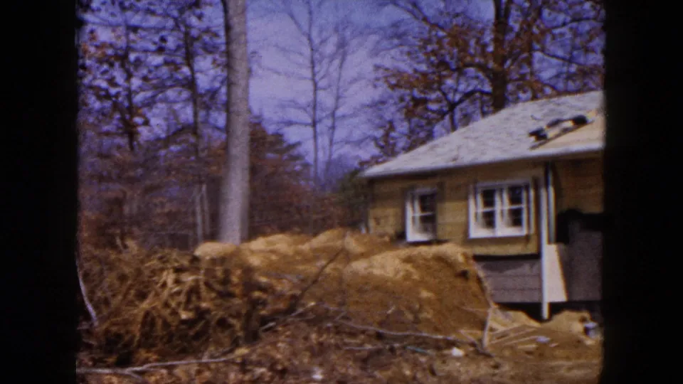 1954 Hicksville home-movie frame showing the side of the house during renovation, with dirt piles in the foreground and exposed siding near the roofline.